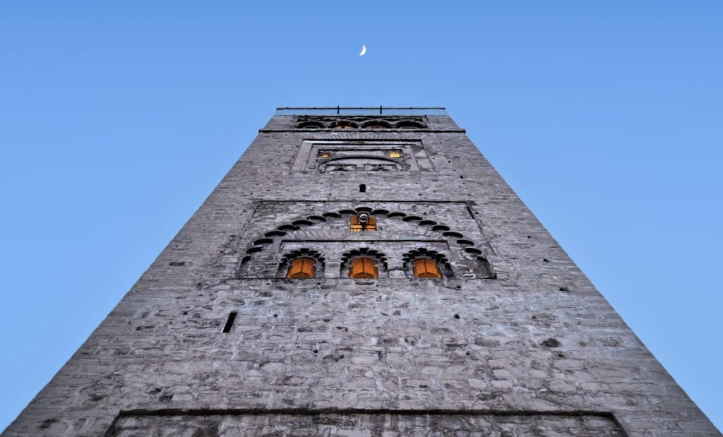 Low angle view of Koutoubia Mosque minaret under a crescent moon and clear sky in Marrakech.