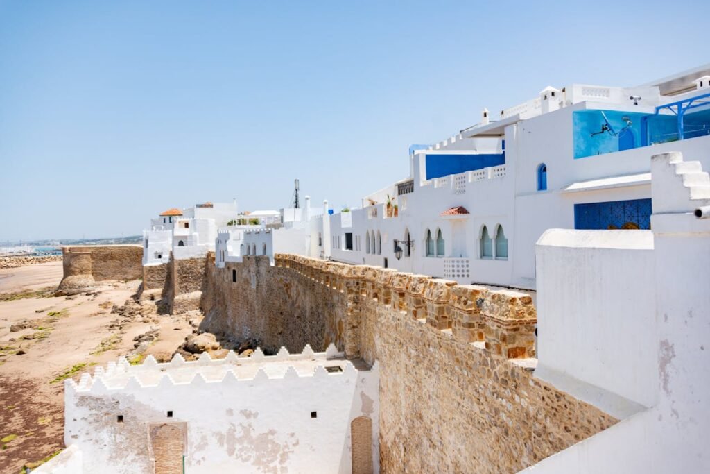 A view of a whitewashed medina with an ancient seaside fortress under a clear blue sky in Morocco.