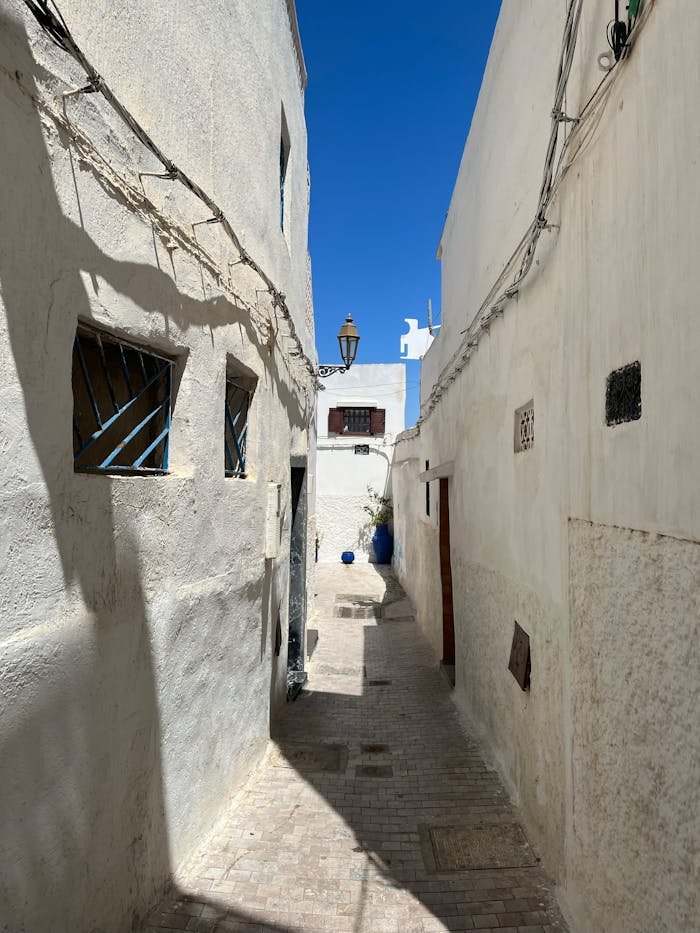 A tranquil narrow alleyway with whitewashed walls under a clear blue sky.
