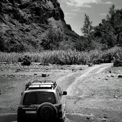 Grayscale SUV crossing a dirt road with mountains in Ouarzazate, Morocco.