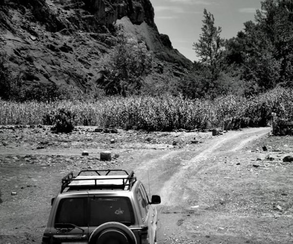 Grayscale SUV crossing a dirt road with mountains in Ouarzazate, Morocco.