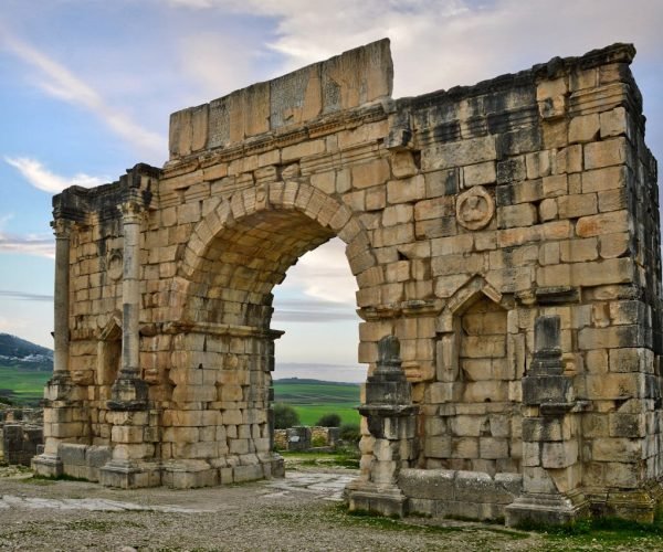 Stunning view of the ancient Roman arch in Volubilis, Morocco amid a serene landscape.