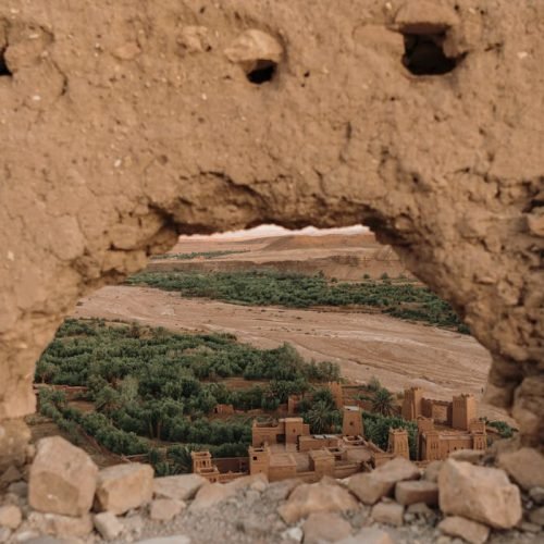 View of Ouarzazate through a traditional mudbrick wall, showcasing historic architecture.