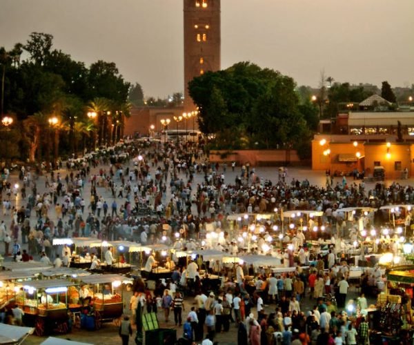 Evening view of bustling Jemaa El-Fnaa market square in Marrakech, Morocco, illuminated with vibrant lights.