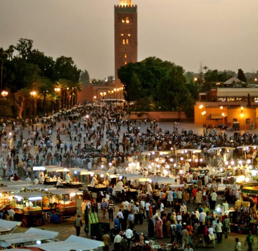 Evening view of bustling Jemaa El-Fnaa market square in Marrakech, Morocco, illuminated with vibrant lights.