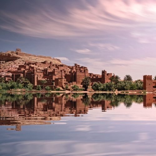 Picturesque reflection of Ouarzazate's historic ksar by the river under a vibrant sky.