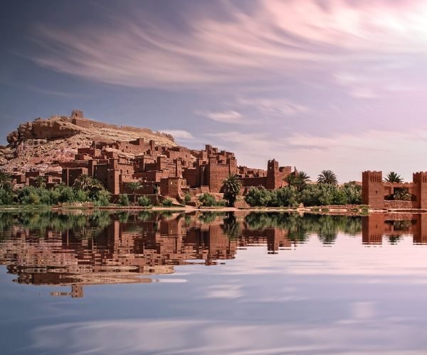 Picturesque reflection of Ouarzazate's historic ksar by the river under a vibrant sky.