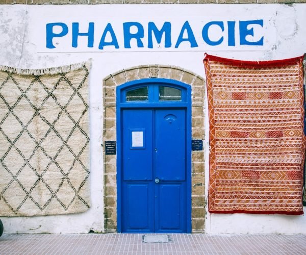 Facade of old pharmacy with bright blue doorway and oriental textile rugs on white shabby wall