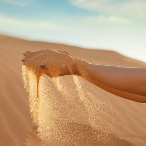A hand releasing fine sand against the vast landscape of Merzouga Sand Dunes, Morocco.