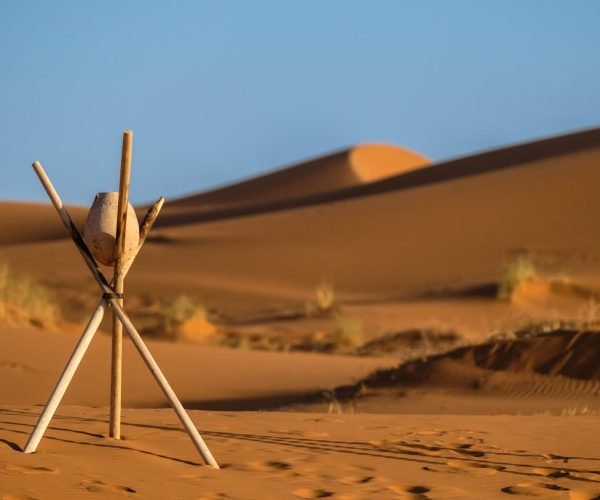 Peaceful desert landscape at Merzouga with sand dunes and wooden tripod under clear blue sky.